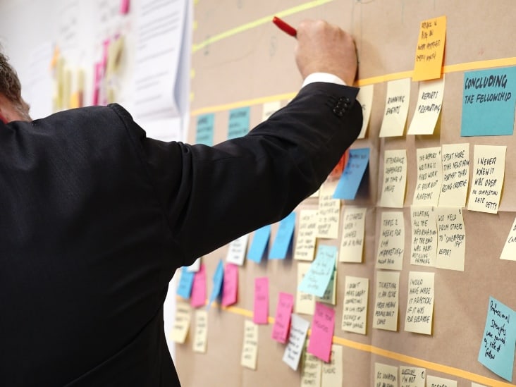 A man writing on a stick note on the card board.
