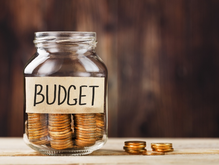 A glass jar with money and labeled "Budget".