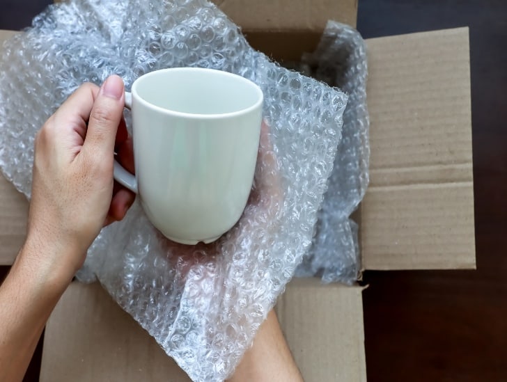 A man wrapping the mug with bubble wrap.