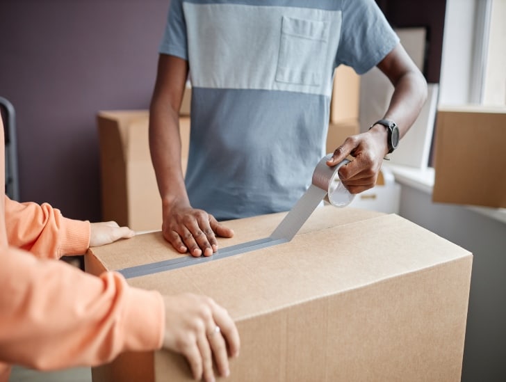 Couple sealing the moving boxes.